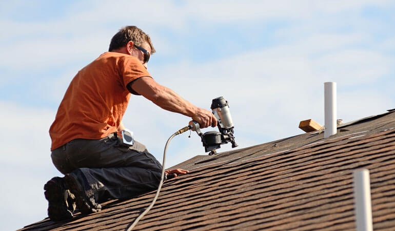 roofer doing asphalt roofing services with drill